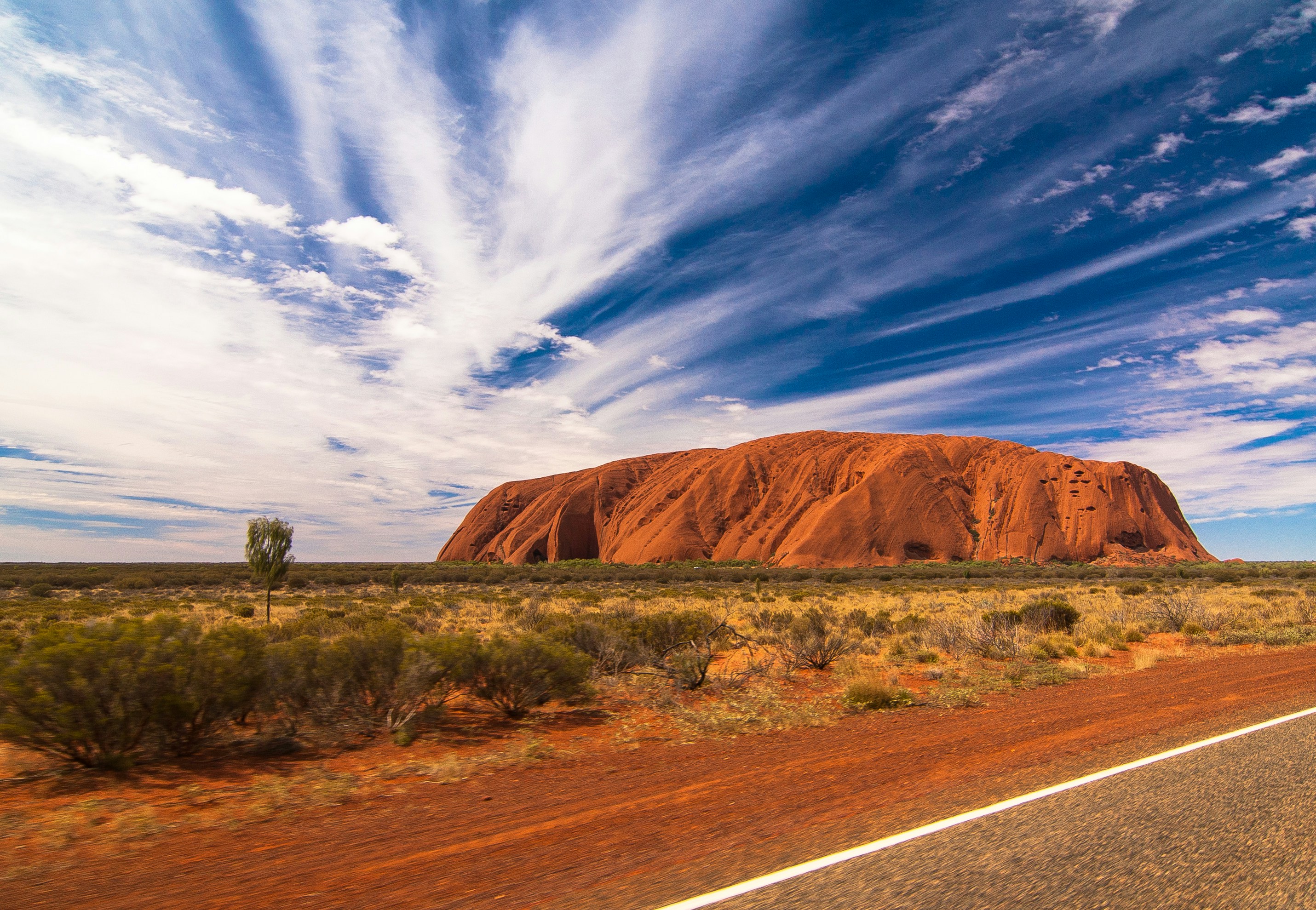The massive red sandstone monolith of Uluru glowing under the deep orange light of a desert sunset