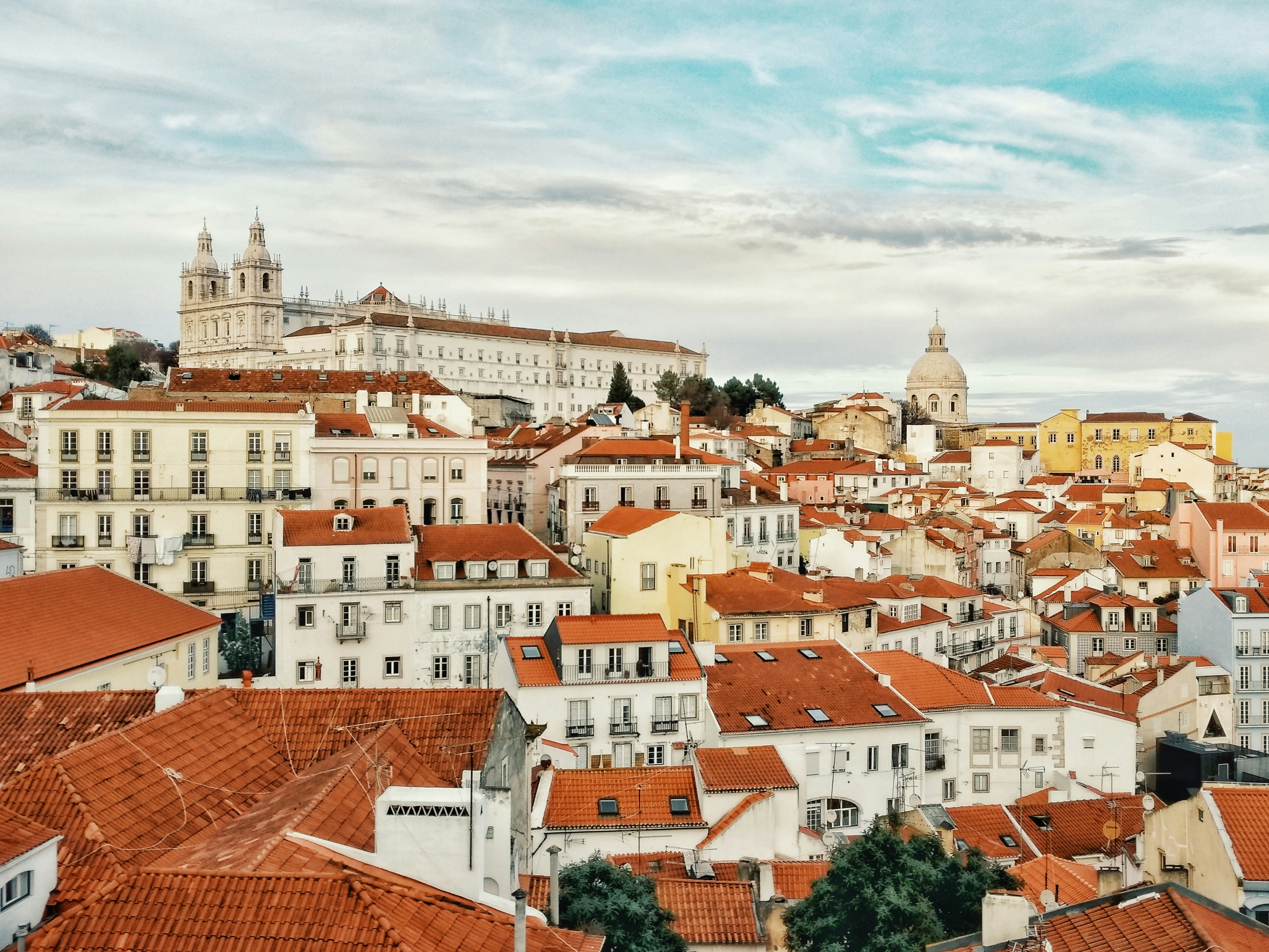 A vintage yellow tram climbing a narrow cobblestone street in the Alfama district of Lisbon, flanked by colorful tiled buildings