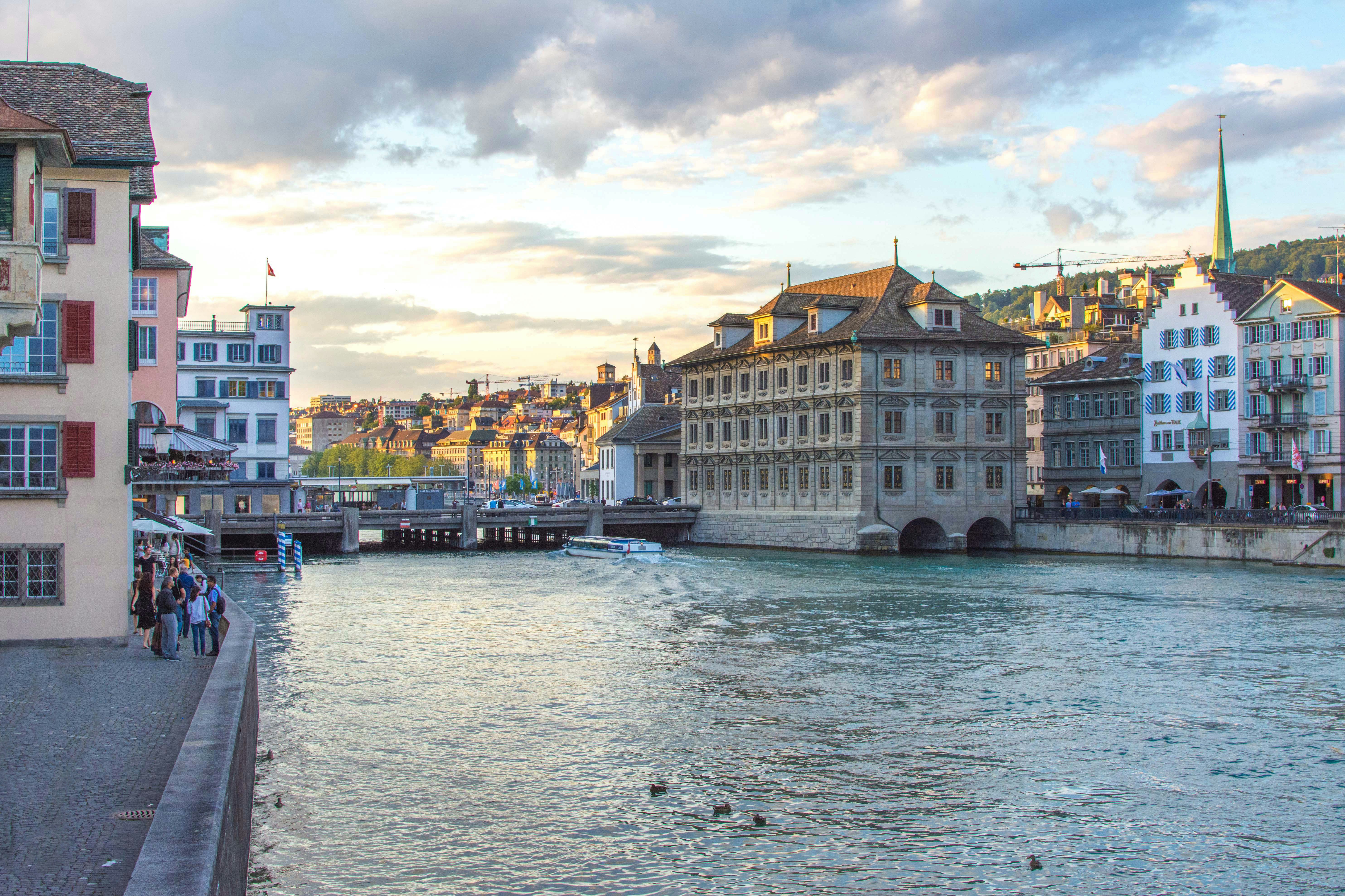 A serene view of Lake Geneva with the Jet d'Eau fountain in the distance and elegant waterfront buildings under a soft sunset